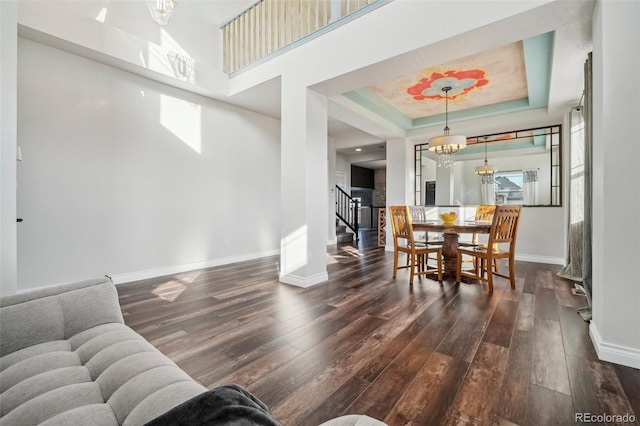 dining space featuring a towering ceiling, dark hardwood / wood-style floors, a notable chandelier, and a tray ceiling