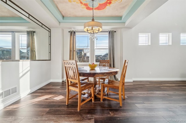 dining room featuring dark wood-type flooring, an inviting chandelier, and a tray ceiling