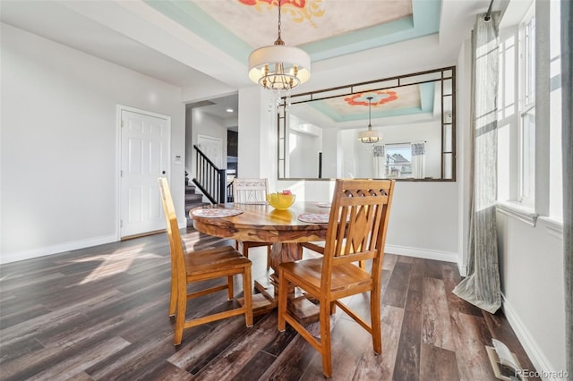 dining space featuring dark hardwood / wood-style flooring, a raised ceiling, and a chandelier