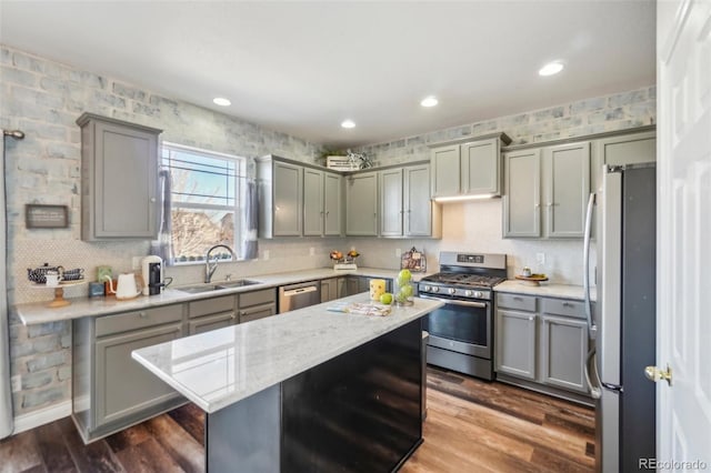 kitchen featuring sink, stainless steel appliances, light stone countertops, a kitchen island, and dark hardwood / wood-style flooring