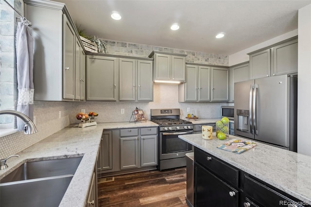 kitchen with dark wood-type flooring, sink, appliances with stainless steel finishes, light stone countertops, and backsplash