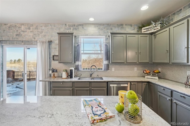 kitchen featuring light stone counters, stainless steel dishwasher, sink, and backsplash