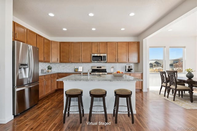 kitchen with light stone countertops, stainless steel appliances, a kitchen breakfast bar, dark hardwood / wood-style flooring, and a kitchen island with sink