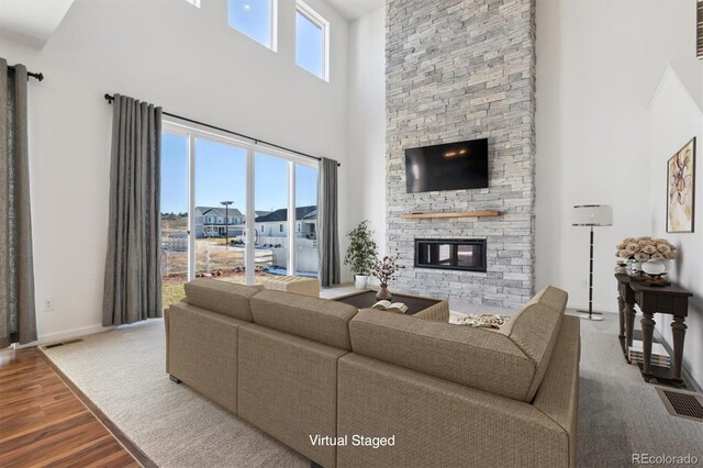 living room featuring a stone fireplace, wood-type flooring, and a high ceiling