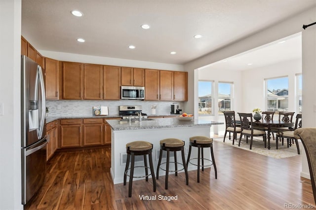 kitchen with a breakfast bar, a center island with sink, dark hardwood / wood-style floors, and appliances with stainless steel finishes