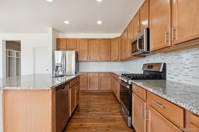 kitchen featuring sink, light stone counters, dark hardwood / wood-style flooring, an island with sink, and appliances with stainless steel finishes