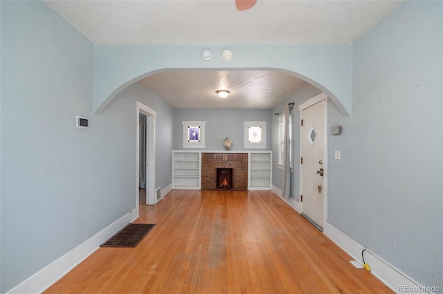 foyer entrance with baseboards, visible vents, light wood finished floors, arched walkways, and a brick fireplace