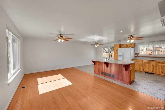 kitchen with white refrigerator with ice dispenser, a breakfast bar area, light countertops, a kitchen island with sink, and a sink