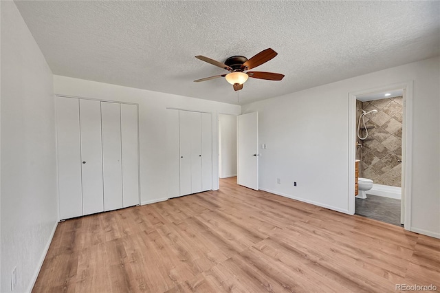 unfurnished bedroom with a textured ceiling, light wood-style floors, baseboards, multiple closets, and ensuite bath