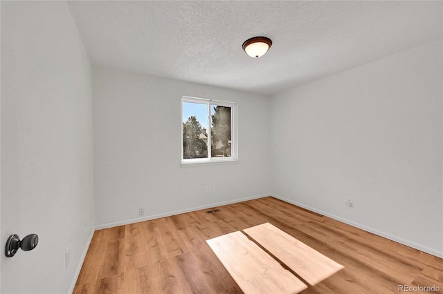 spare room featuring light wood-type flooring, visible vents, a textured ceiling, and baseboards