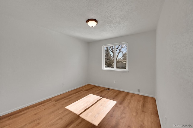 unfurnished room with baseboards, a textured ceiling, visible vents, and light wood-style floors