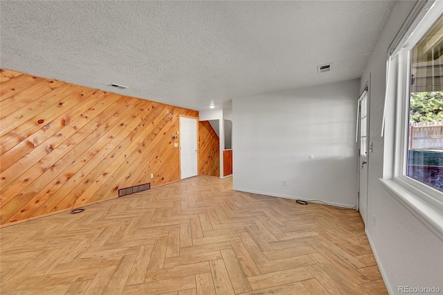 empty room with visible vents, wooden walls, and a textured ceiling