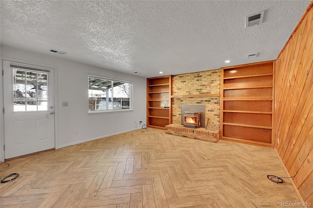 unfurnished living room with built in features, a wood stove, visible vents, and a textured ceiling