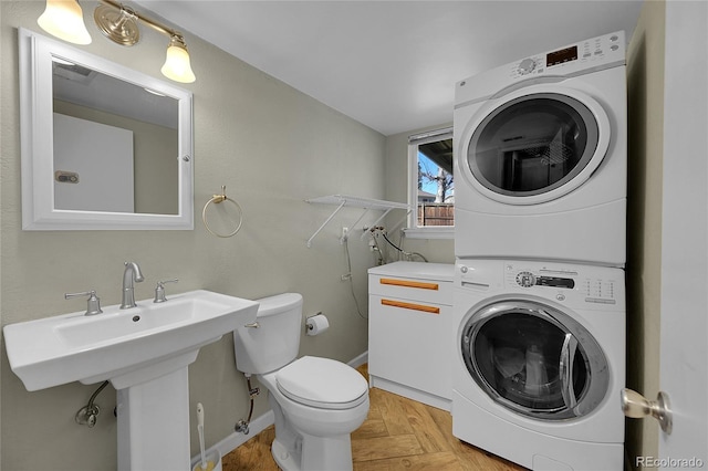 washroom with laundry area, baseboards, a sink, and stacked washing maching and dryer