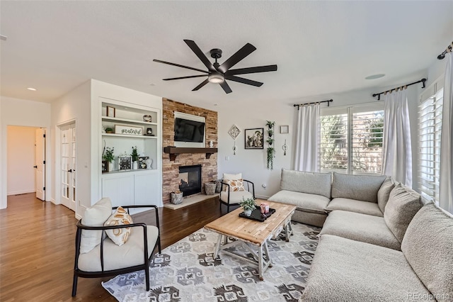 living room with a fireplace, ceiling fan, built in shelves, and hardwood / wood-style flooring