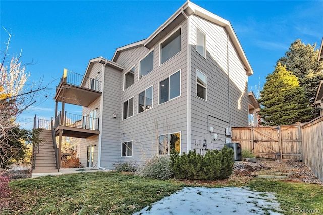 back of property with a lawn, a balcony, and central AC