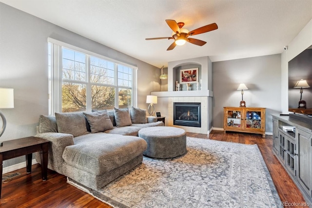 living room featuring dark hardwood / wood-style flooring, a tiled fireplace, and ceiling fan