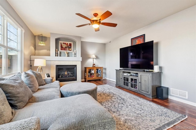 living room with dark wood-type flooring, ceiling fan, and a tiled fireplace