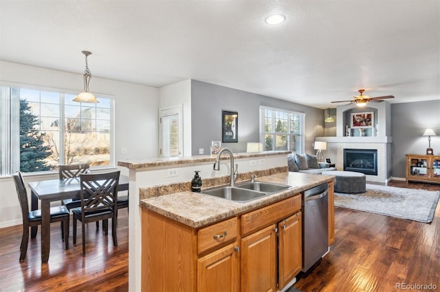 kitchen featuring sink, dishwasher, a kitchen island with sink, hanging light fixtures, and a large fireplace