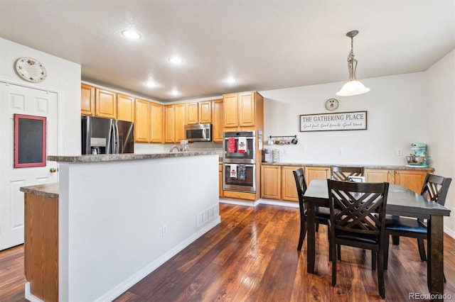 kitchen with pendant lighting, dark wood-type flooring, appliances with stainless steel finishes, a kitchen island, and light brown cabinets