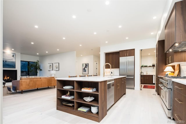 kitchen with a fireplace, premium range hood, a center island with sink, sink, and high quality appliances