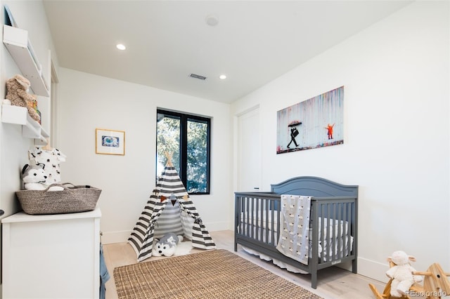 bedroom with light hardwood / wood-style floors and a nursery area