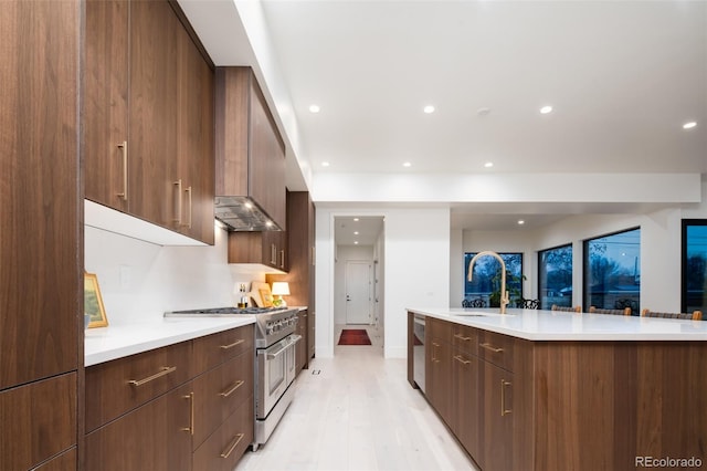 kitchen with appliances with stainless steel finishes, light hardwood / wood-style floors, sink, backsplash, and a center island with sink