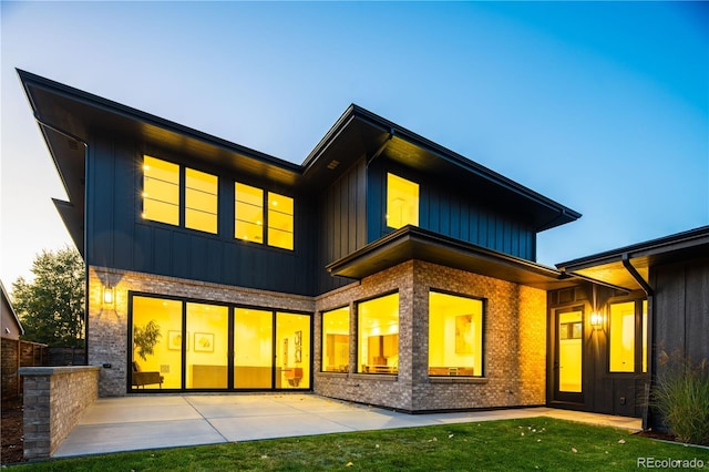 rear view of house featuring board and batten siding, a patio area, and brick siding