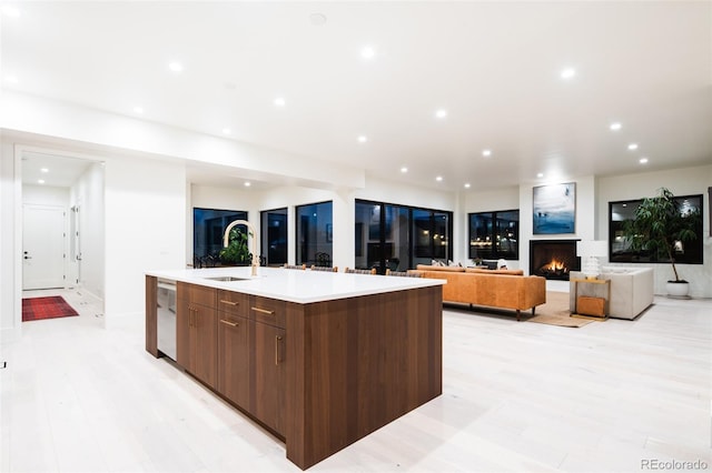 kitchen with light wood finished floors, modern cabinets, a lit fireplace, a large island with sink, and a sink