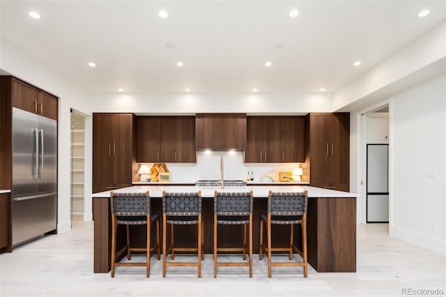 kitchen featuring built in fridge, light countertops, modern cabinets, a large island with sink, and built in refrigerator