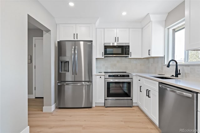 kitchen with appliances with stainless steel finishes, light hardwood / wood-style floors, tasteful backsplash, white cabinets, and sink