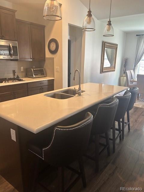 kitchen featuring stainless steel appliances, hanging light fixtures, sink, and a center island with sink