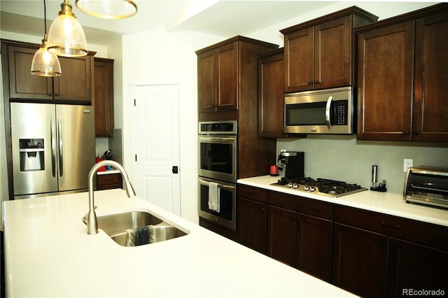 kitchen with a sink, stainless steel appliances, light countertops, decorative light fixtures, and tasteful backsplash