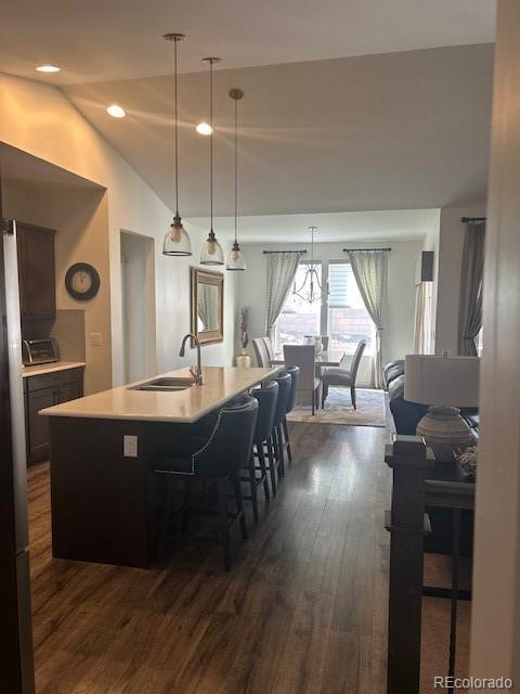 kitchen with dark wood finished floors, pendant lighting, light countertops, vaulted ceiling, and a sink