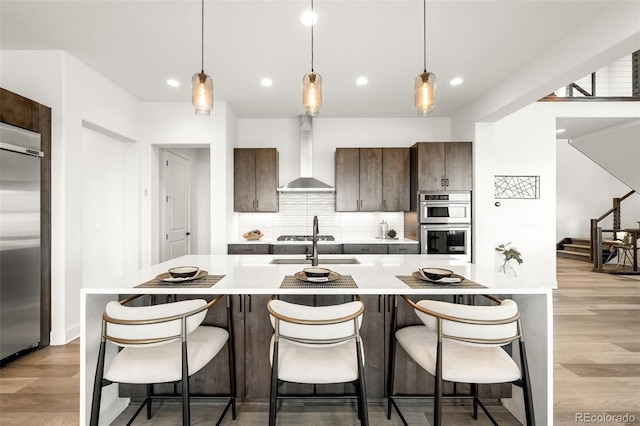16262 W 95th Ln, Arvada, CO 80007 - kitchen featuring wall chimney range hood, appliances with stainless steel finishes, light wood finished floors, tasteful backsplash, and light countertops