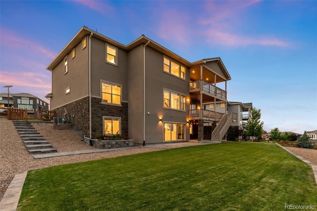 16262 W 95th Ln, Arvada, CO 80007 - back of house at dusk with stairway, a balcony, stucco siding, a lawn, and stone siding