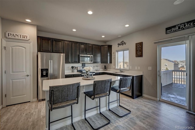 kitchen with dark brown cabinetry, a center island, light hardwood / wood-style flooring, appliances with stainless steel finishes, and a kitchen breakfast bar