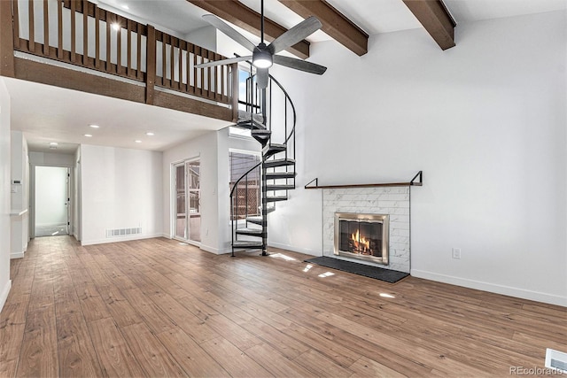 unfurnished living room featuring wood finished floors, visible vents, stairway, beamed ceiling, and ceiling fan