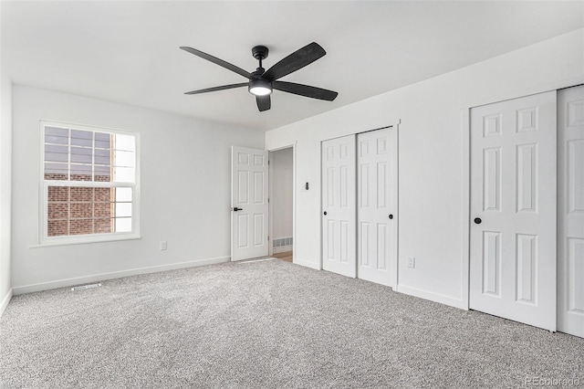 unfurnished bedroom with two closets, carpet floors, and baseboards