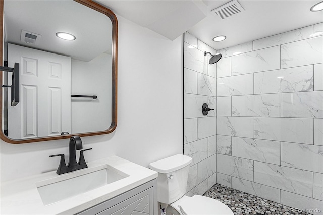 bathroom featuring toilet, tiled shower, vanity, and visible vents