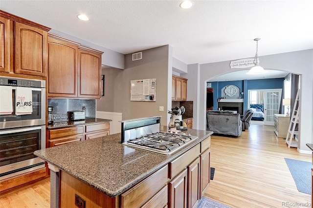 9994 Quintero St, Commerce City, CO 80022 - kitchen featuring stainless steel appliances, arched walkways, a kitchen island, light wood-style flooring, and recessed lighting