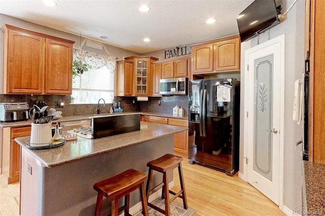 9994 Quintero St, Commerce City, CO 80022 - kitchen featuring black fridge with ice dispenser, stainless steel microwave, light wood-style floors, a sink, and a breakfast bar