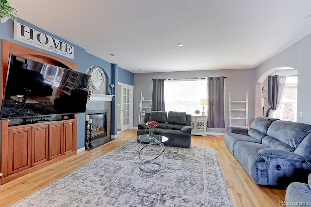9994 Quintero St, Commerce City, CO 80022 - living room with arched walkways, light wood finished floors, a tiled fireplace, and baseboards