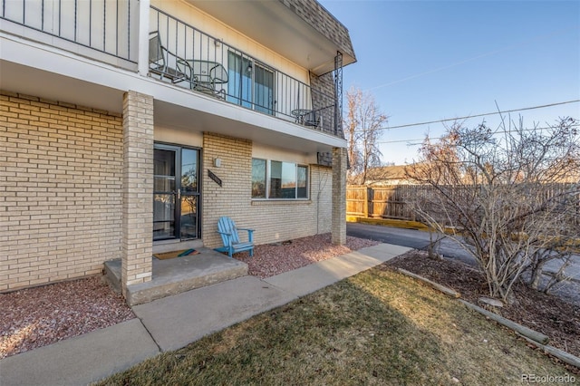 exterior space with board and batten siding, brick siding, fence, and a balcony