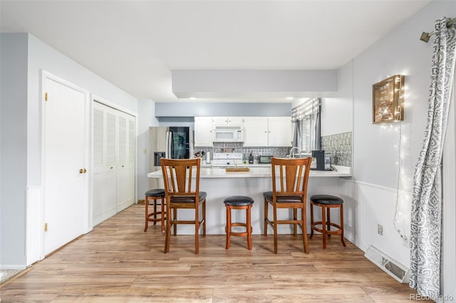 kitchen featuring light wood finished floors, visible vents, backsplash, white microwave, and a peninsula