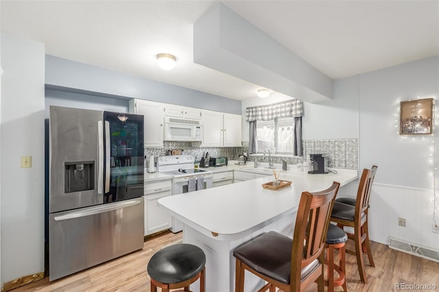 kitchen with a peninsula, white appliances, a sink, visible vents, and a kitchen bar