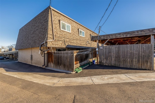 exterior space with mansard roof, roof with shingles, fence, and brick siding