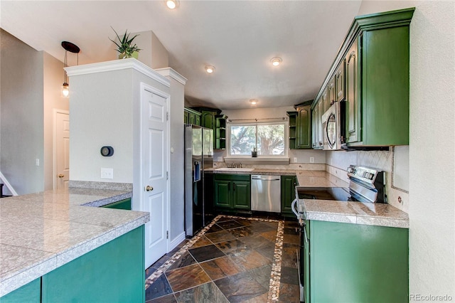 kitchen featuring appliances with stainless steel finishes, green cabinets, tile counters, a sink, and stone tile flooring