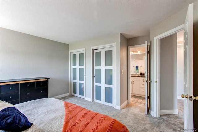 bedroom featuring light colored carpet, two closets, baseboards, a textured ceiling, and french doors