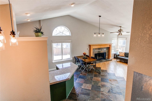 dining room featuring ceiling fan, lofted ceiling, dark stone finish flooring, a tiled fireplace, and plenty of natural light